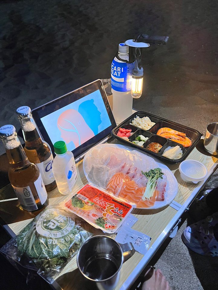 맹방해변 모래사장에 편 상 위의 포장 회와 맥주, 충전식 랜턴